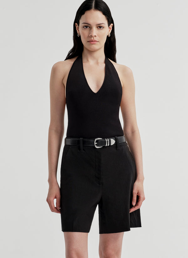 Woman wearing a black halter bodysuit and black shorts on a light gray background