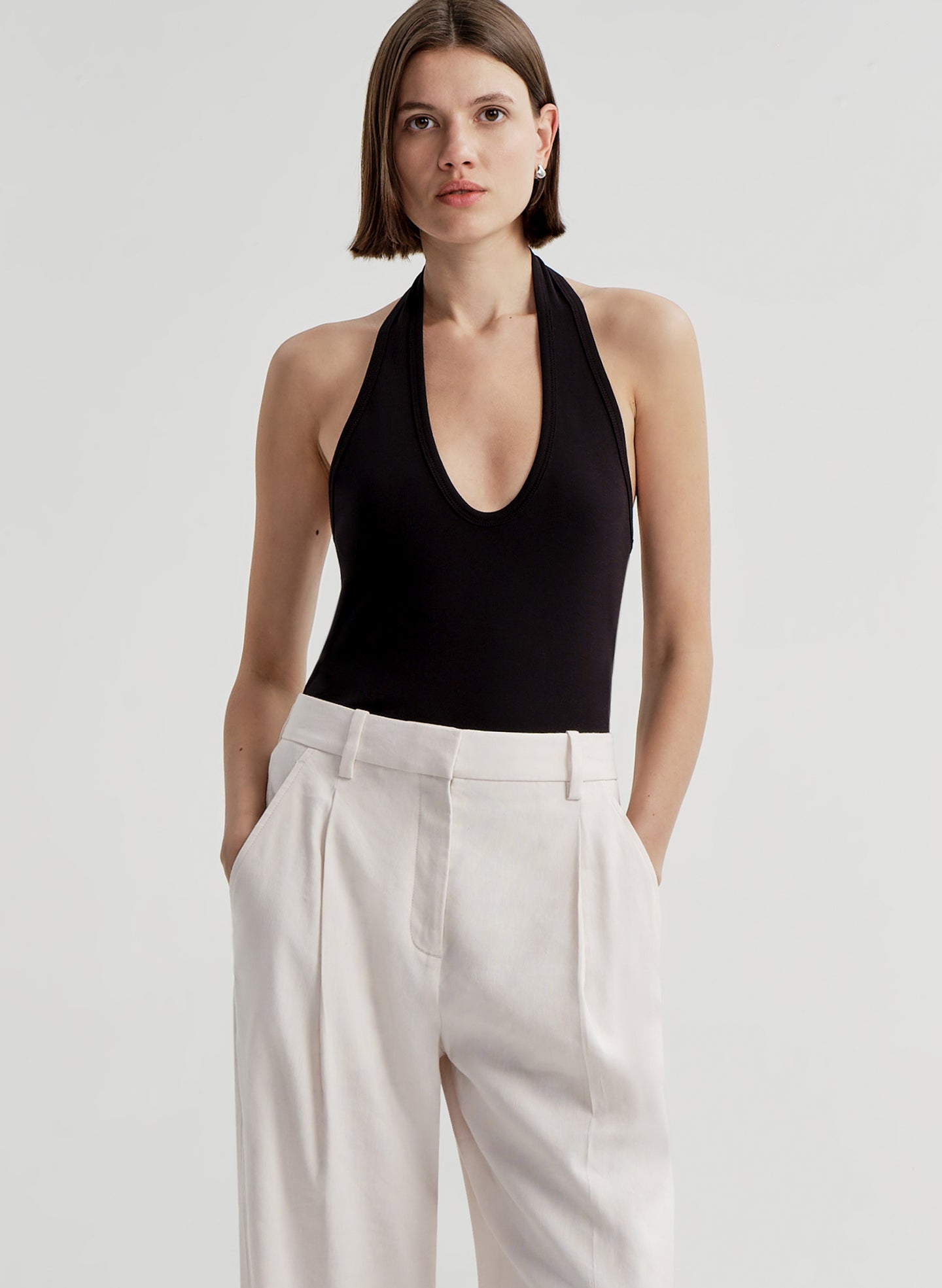 Woman wearing a black halter top and light colored pants on a light gray background