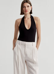 Woman wearing a black halter top and light colored pants on a light gray background