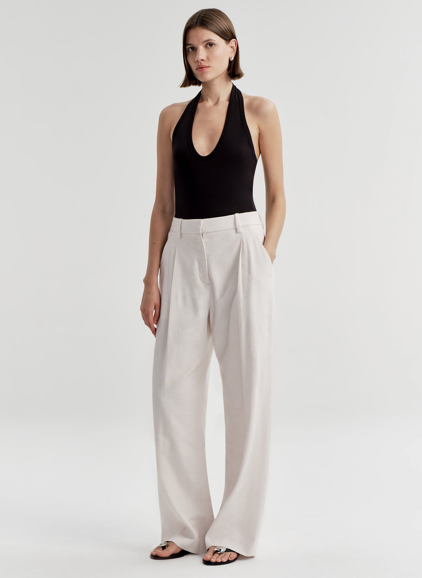 Woman wearing a black halter top and light colored pants on a light gray background