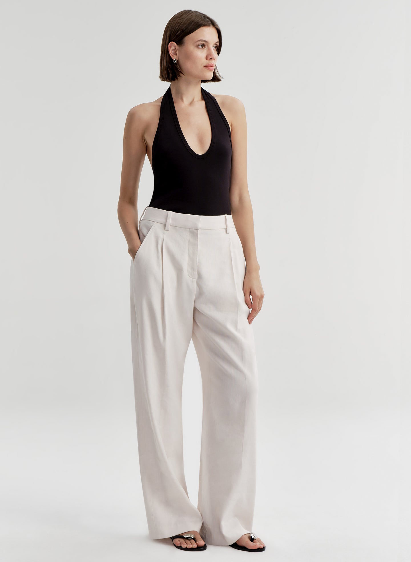 Woman wearing a black halter top and light colored pants on a light gray background