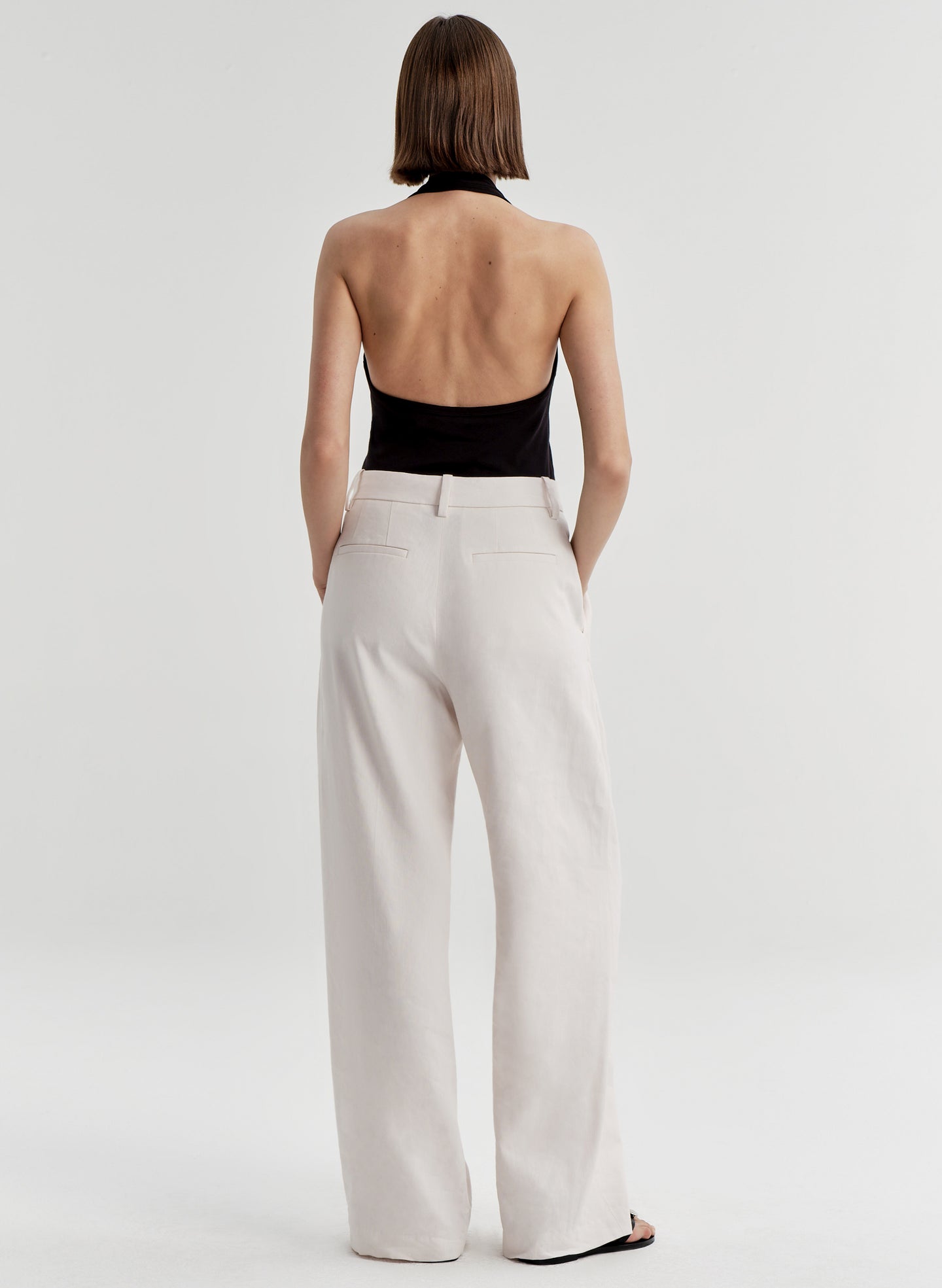Woman wearing a black halter top and light colored pants on a light gray background