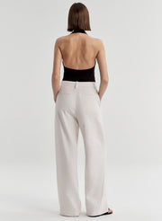 Woman wearing a black halter top and light colored pants on a light gray background