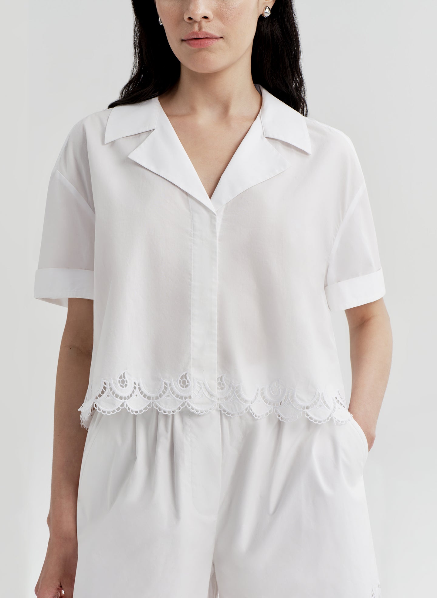 Woman wearing a white top with lace details and matching shorts on a plain background