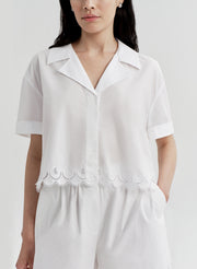 Woman wearing a white top with lace details and matching shorts on a plain background