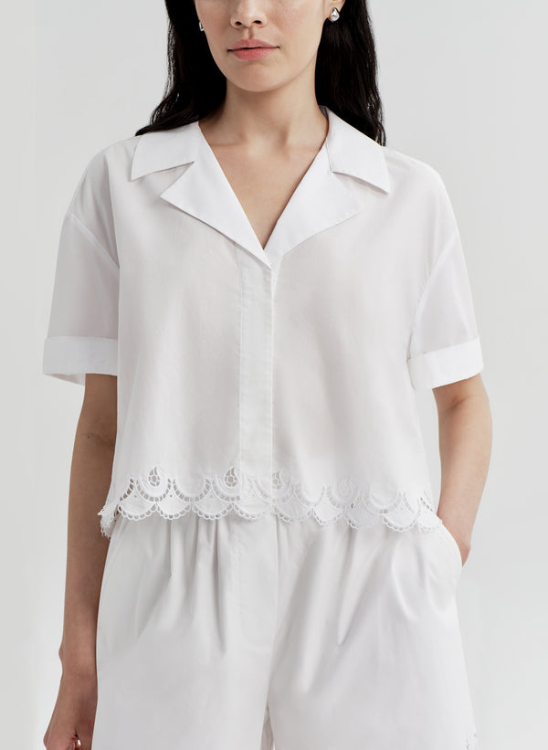 Woman wearing a white top with lace details and matching shorts on a plain background