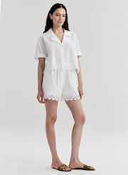 Woman wearing a white top with lace details and matching shorts on a plain background