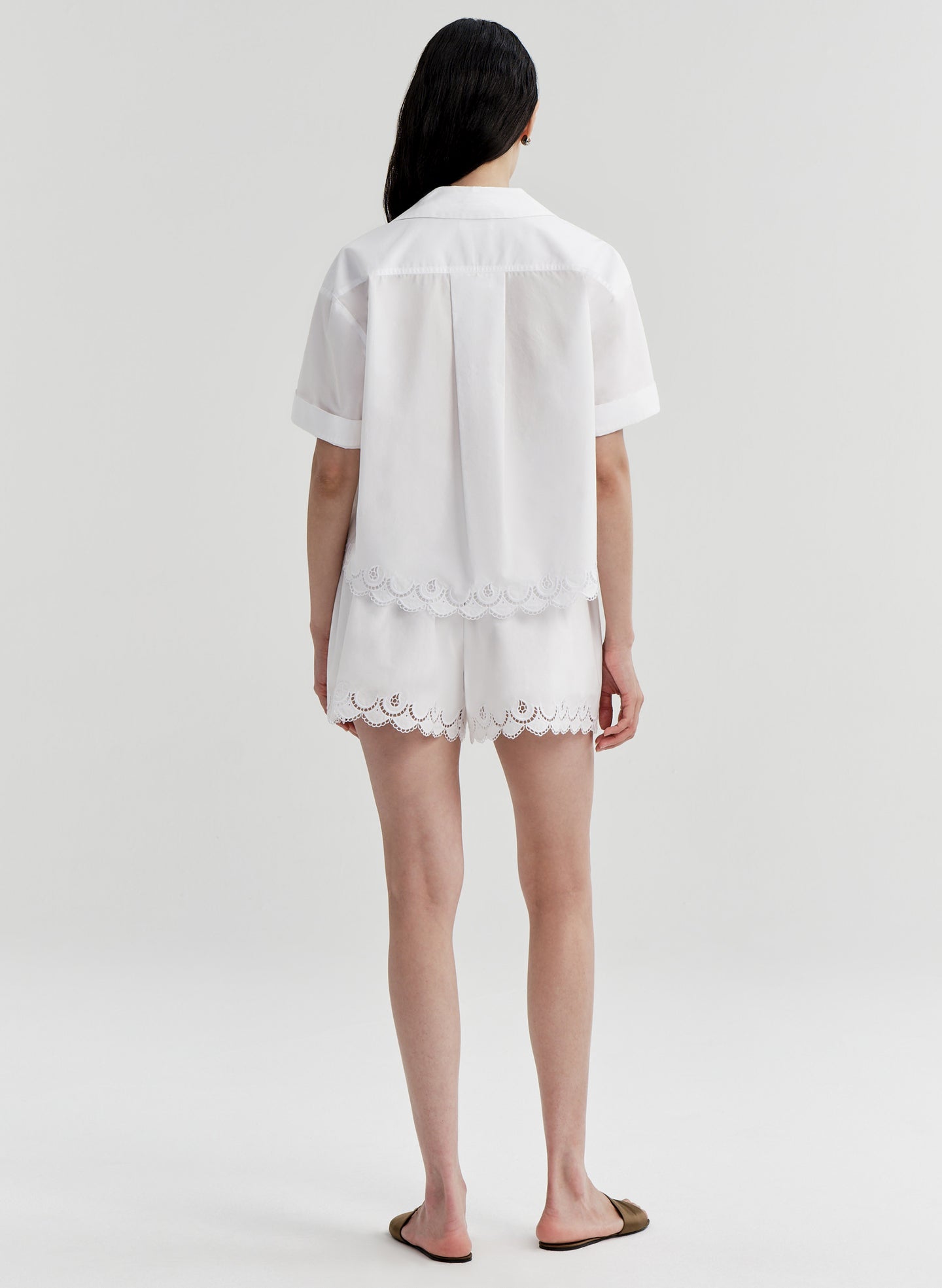 Woman wearing a white top with lace details and matching shorts on a plain background