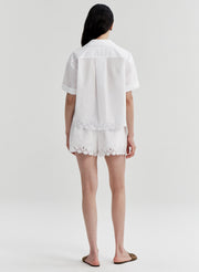 Woman wearing a white top with lace details and matching shorts on a plain background