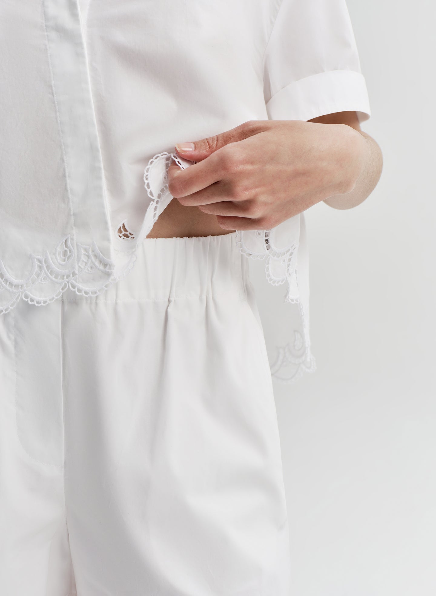 Close-up of a person woman wearing white embroidered short with a matching top on a light gray background