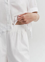 Close-up of a person woman wearing white embroidered short with a matching top on a light gray background