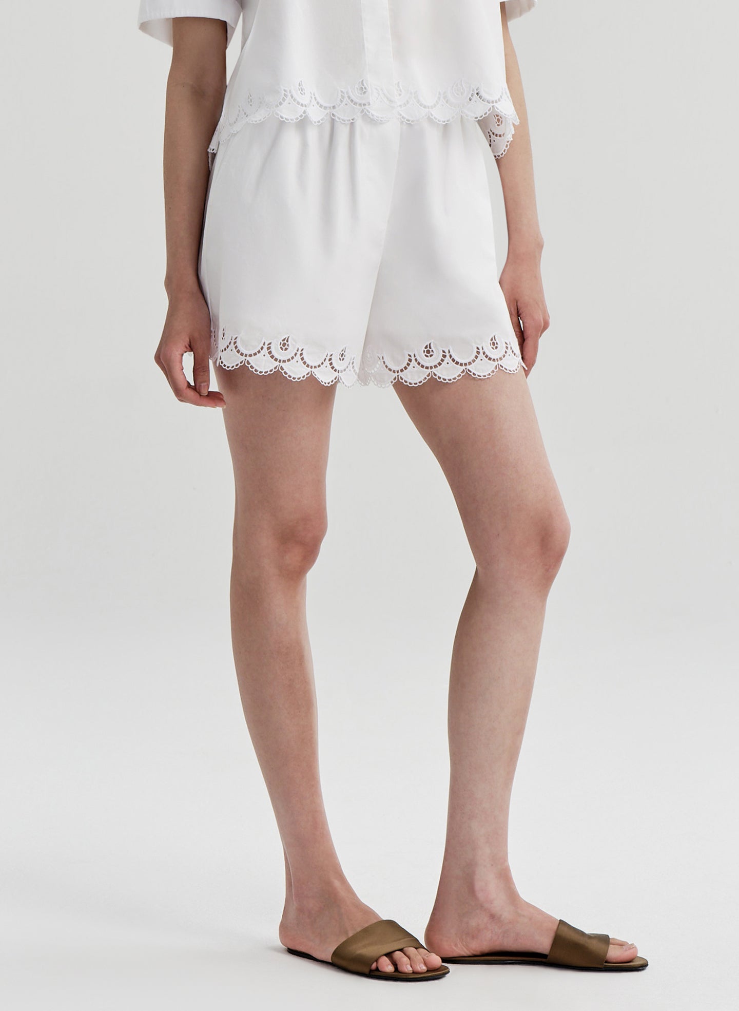 Woman wearing a white lace-trimmed shorts with a matching top on a plain background