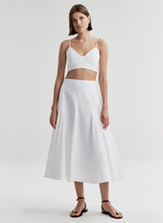 Woman wearing a white skirt and matching top on a plain background