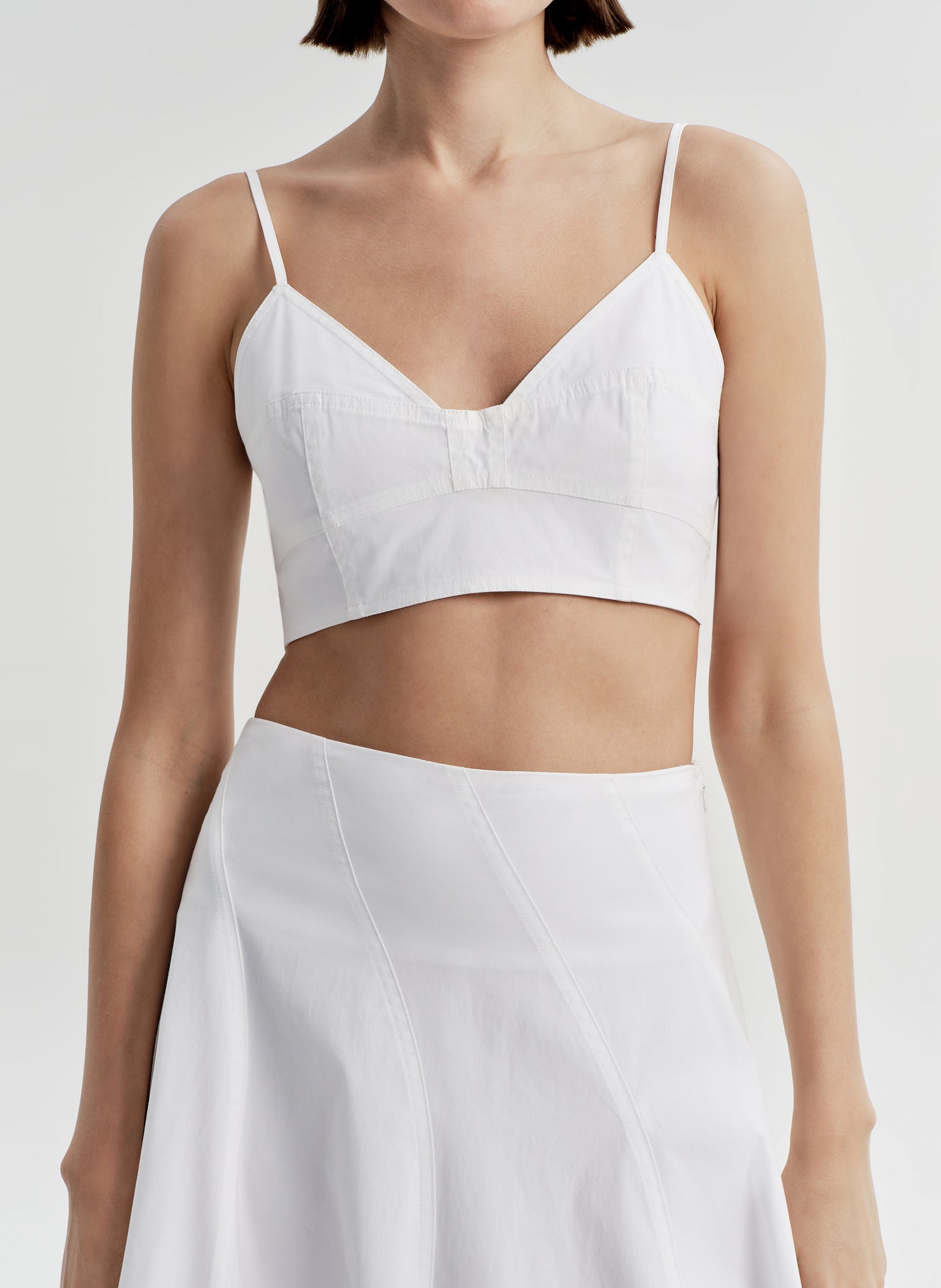Woman wearing a white crop top and matching skirt set on a light gray background