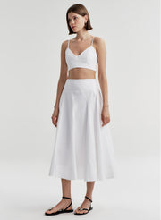 Woman wearing a white crop top and matching skirt set on a light gray background