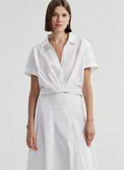 Woman wearing a white collared top with a knot detail on a plain 