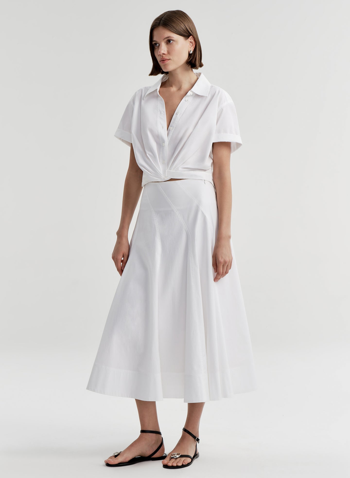 Woman wearing a white collared top with a knot detail on a plain 