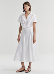 Woman wearing a white collared top with a knot detail on a plain 