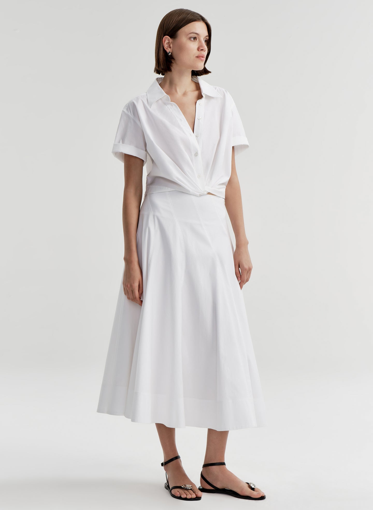 Woman wearing a white collared top with a knot detail on a plain 