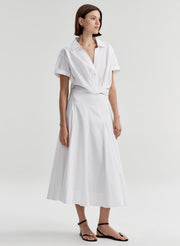 Woman wearing a white collared top with a knot detail on a plain 