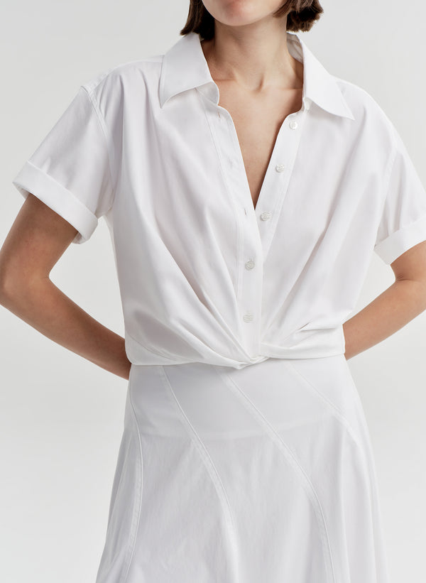 Woman wearing a white collared top with a knot detail on a plain background