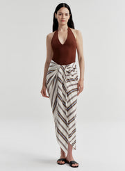 Woman wearing a brown halter top and striped white and black sarong on a plain background