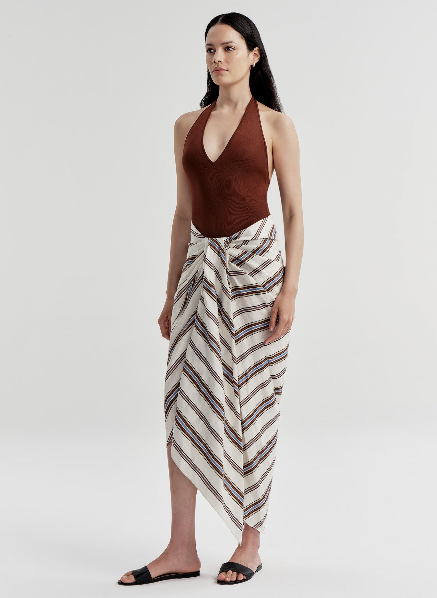 Woman wearing a brown halter top and striped skirt on a white background