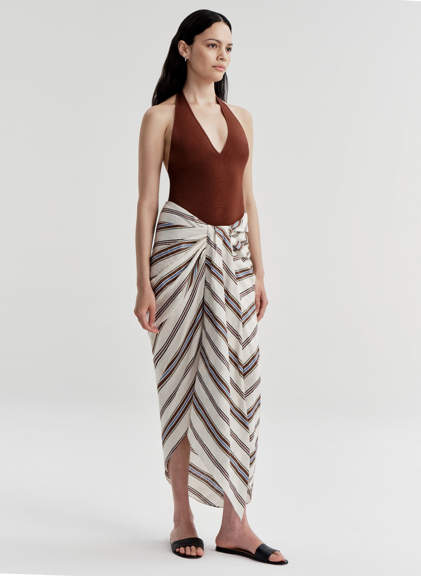 Woman wearing a brown halter top and striped sarong on a white background