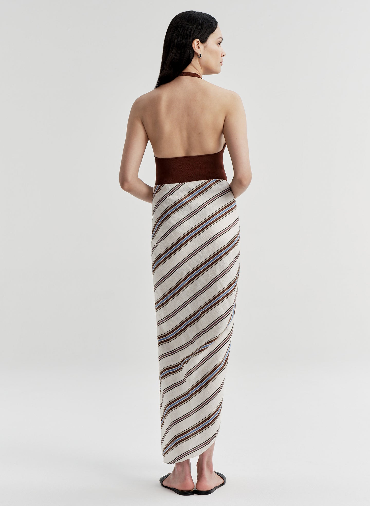 Woman wearing a brown halter top and striped sarong on a white background