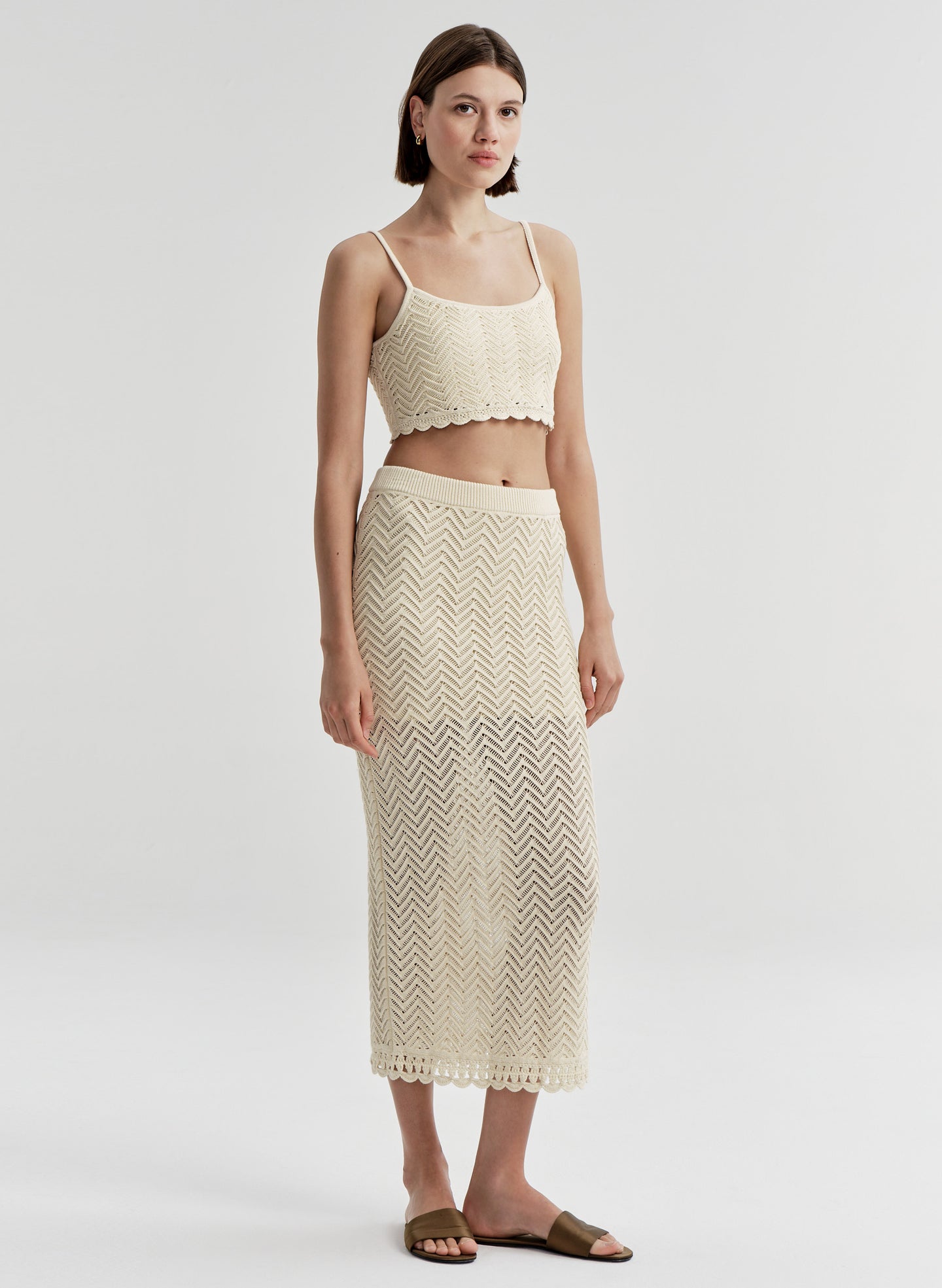 Woman wearing a beige knit cropped top and matching skirt on a light gray background