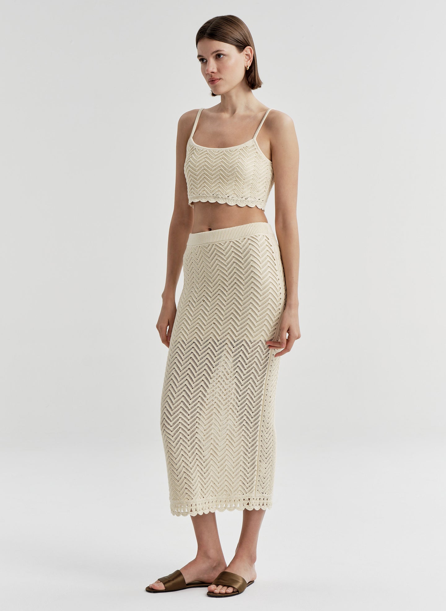Woman wearing a beige knit cropped top and matching skirt on a light gray background