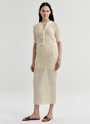 Woman wearing a beige crocheted cardigan and matching skirt on a light gray background