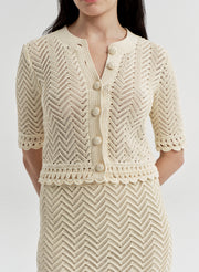 Woman wearing a beige crocheted cardigan and matching skirt on a light gray background