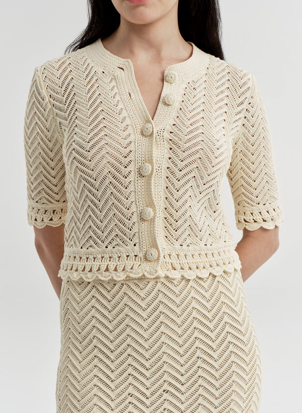 Woman wearing a beige crocheted cardigan and matching skirt on a light gray background