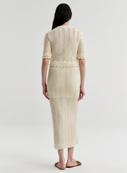 Woman wearing a beige crocheted cardigan and matching skirt on a light gray background