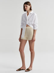 Woman wearing beige knitted shorts with lace trim and a white top with a white background 