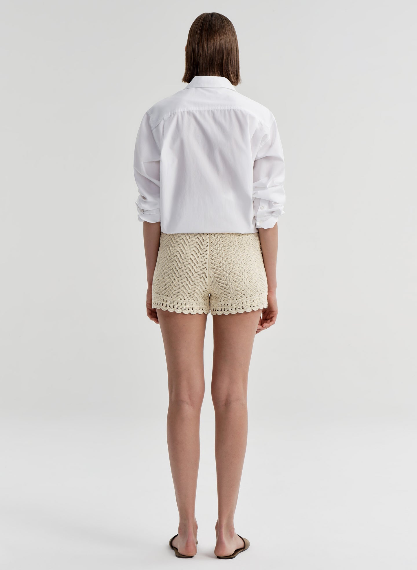 Woman wearing beige knitted shorts with lace trim and a white top with a white background 