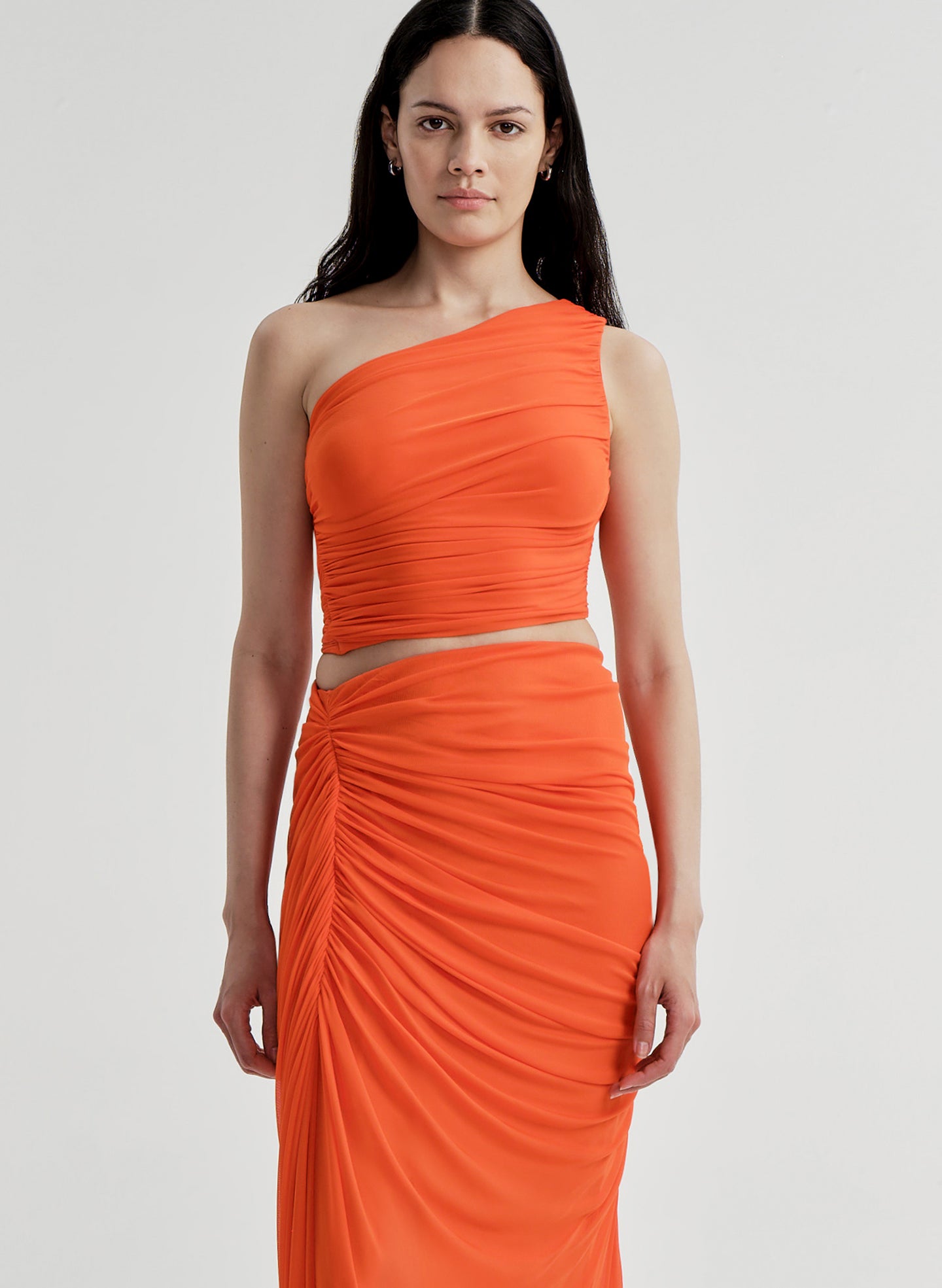 Woman wearing an orange one-shoulder top with a matching skirt on a white background
