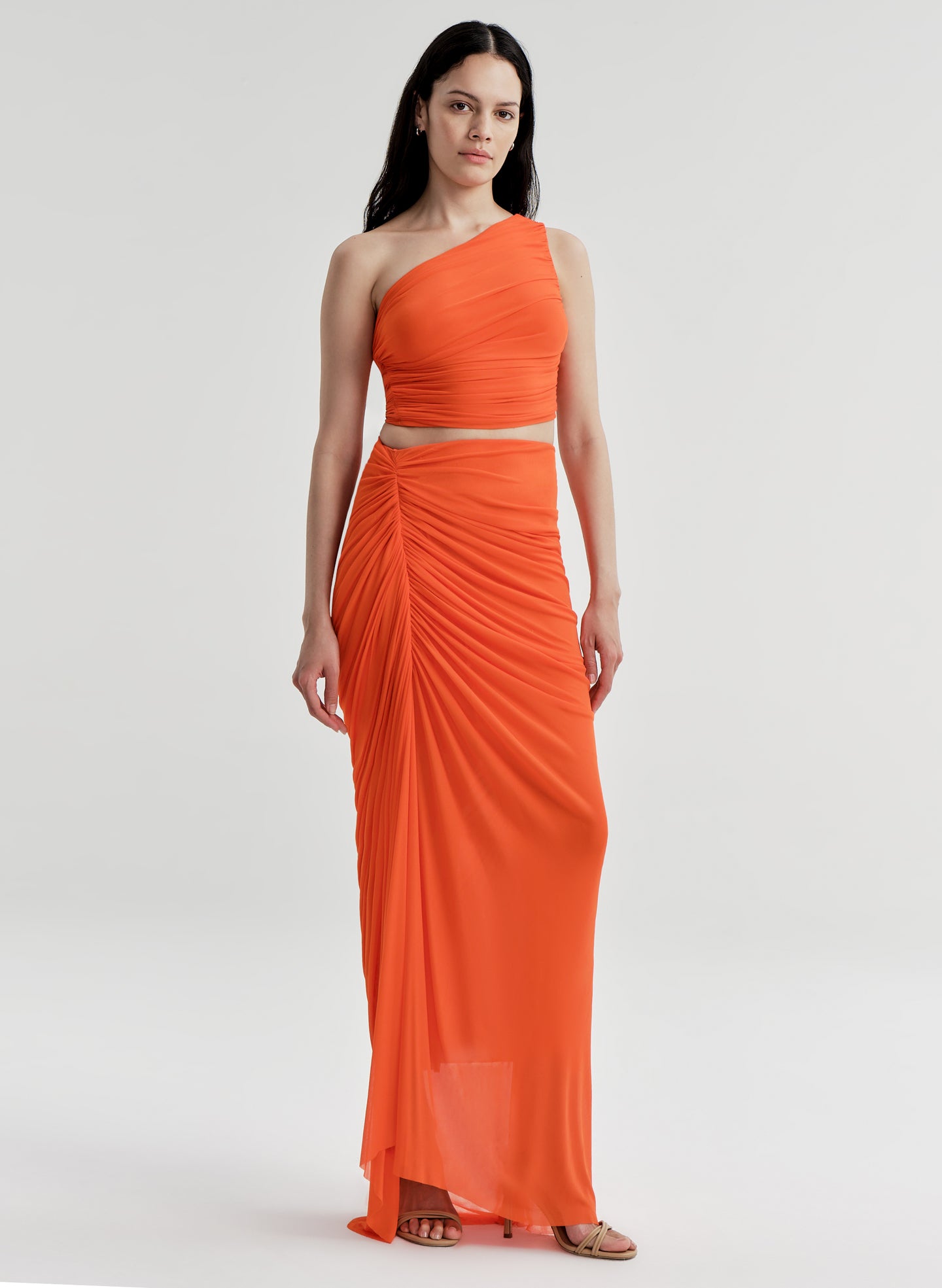 Woman wearing an orange one-shoulder top with a matching skirt on a white background