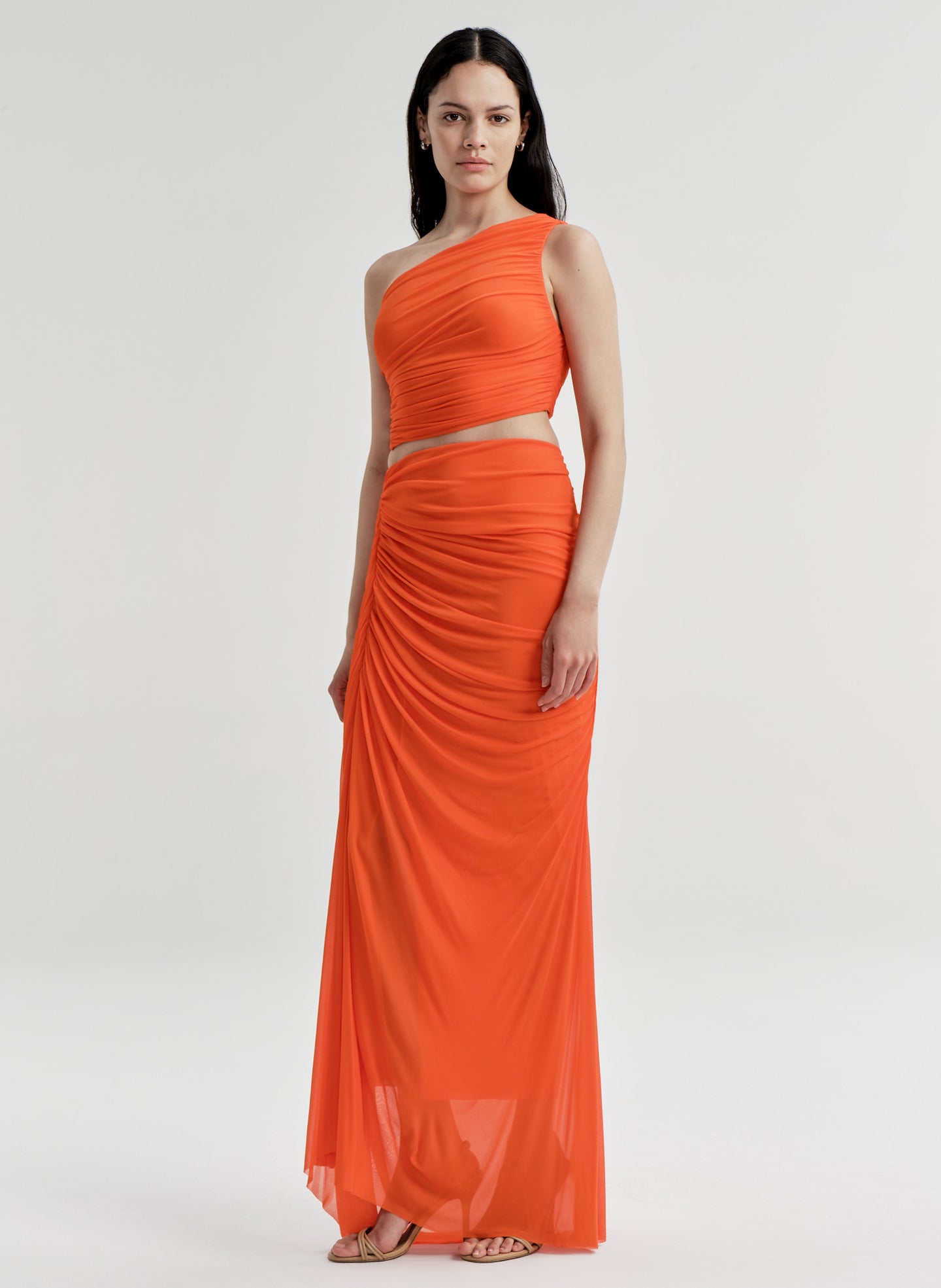 Woman wearing an orange one-shoulder top with a matching skirt on a white background