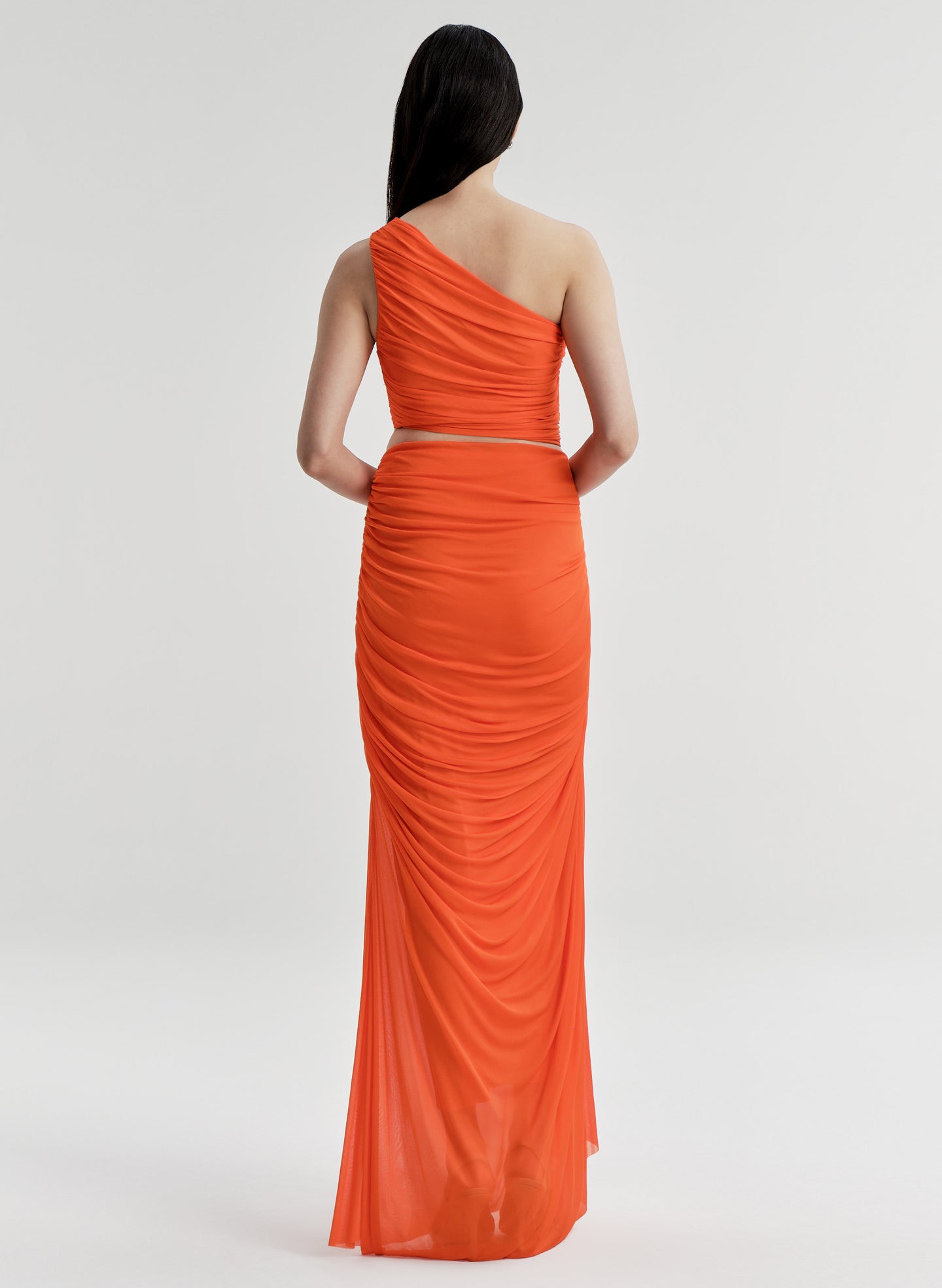 Woman wearing an orange one-shoulder top with a matching skirt on a white background