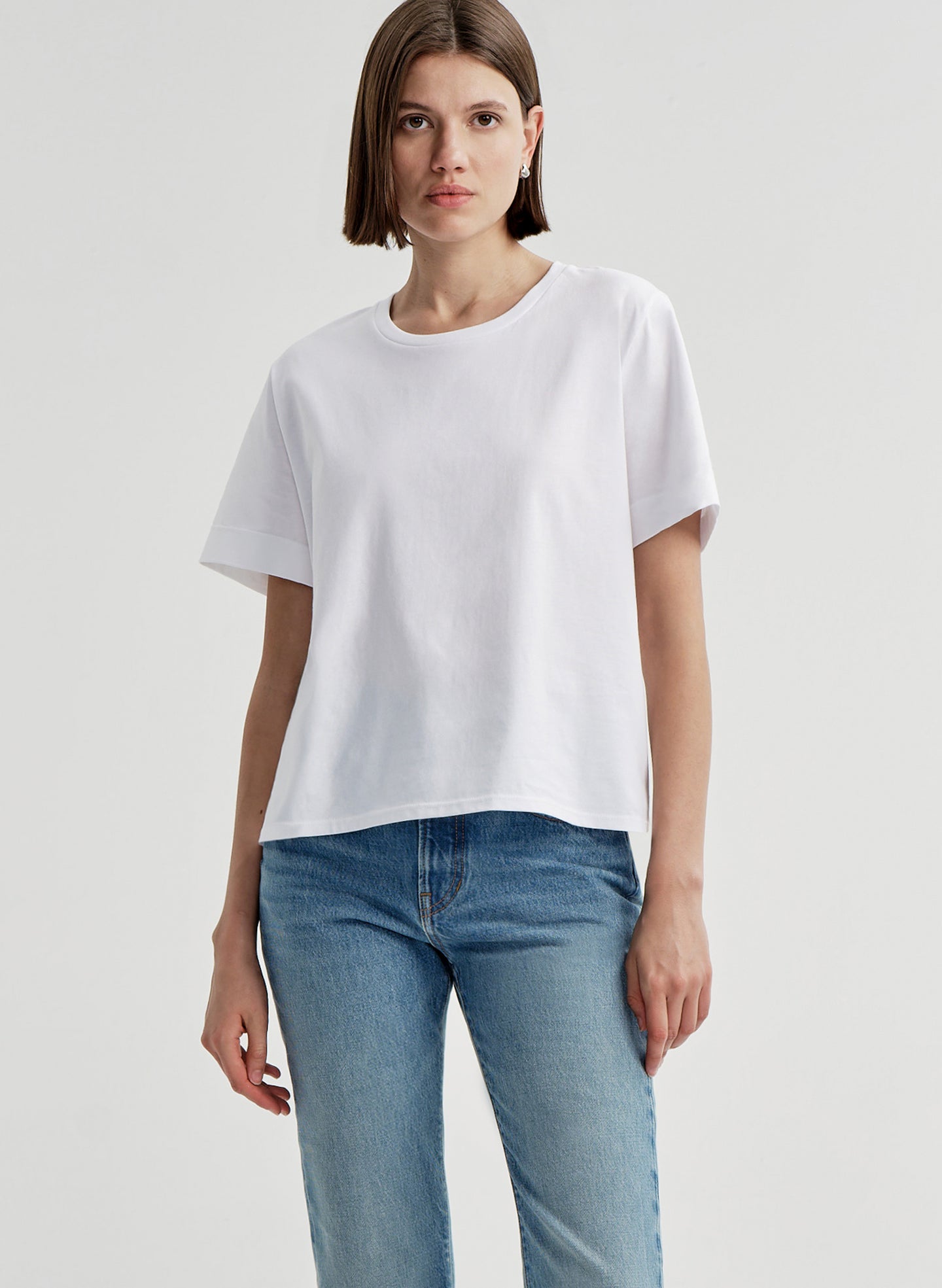 Woman wearing a white t-shirt and blue jeans on a light gray background