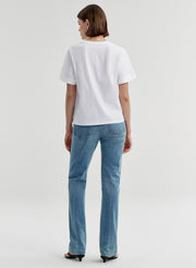 Woman wearing a white t-shirt and blue jeans on a light gray background