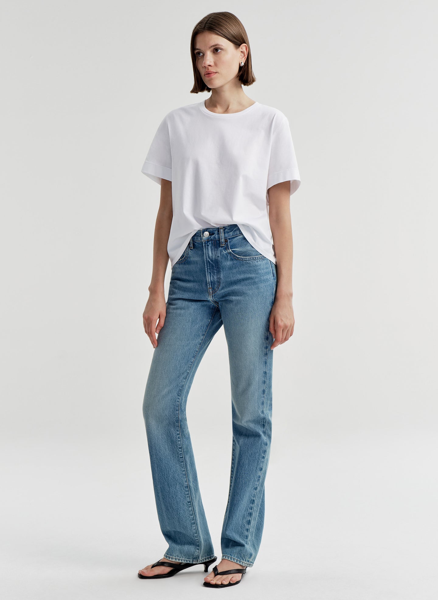 Woman wearing a white t-shirt and blue jeans on a light gray background