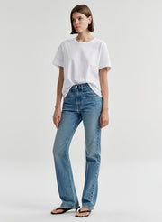 Woman wearing a white t-shirt and blue jeans on a light gray background