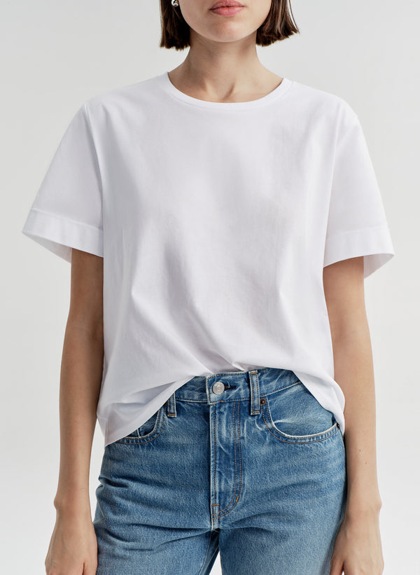 Woman wearing a white t-shirt and blue jeans on a light gray background