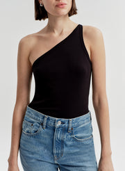 Woman wearing a black one-shoulder top and blue jeans on a light gray background