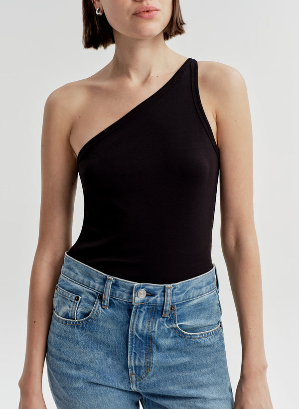 Woman wearing a black one-shoulder top and blue jeans on a light gray background