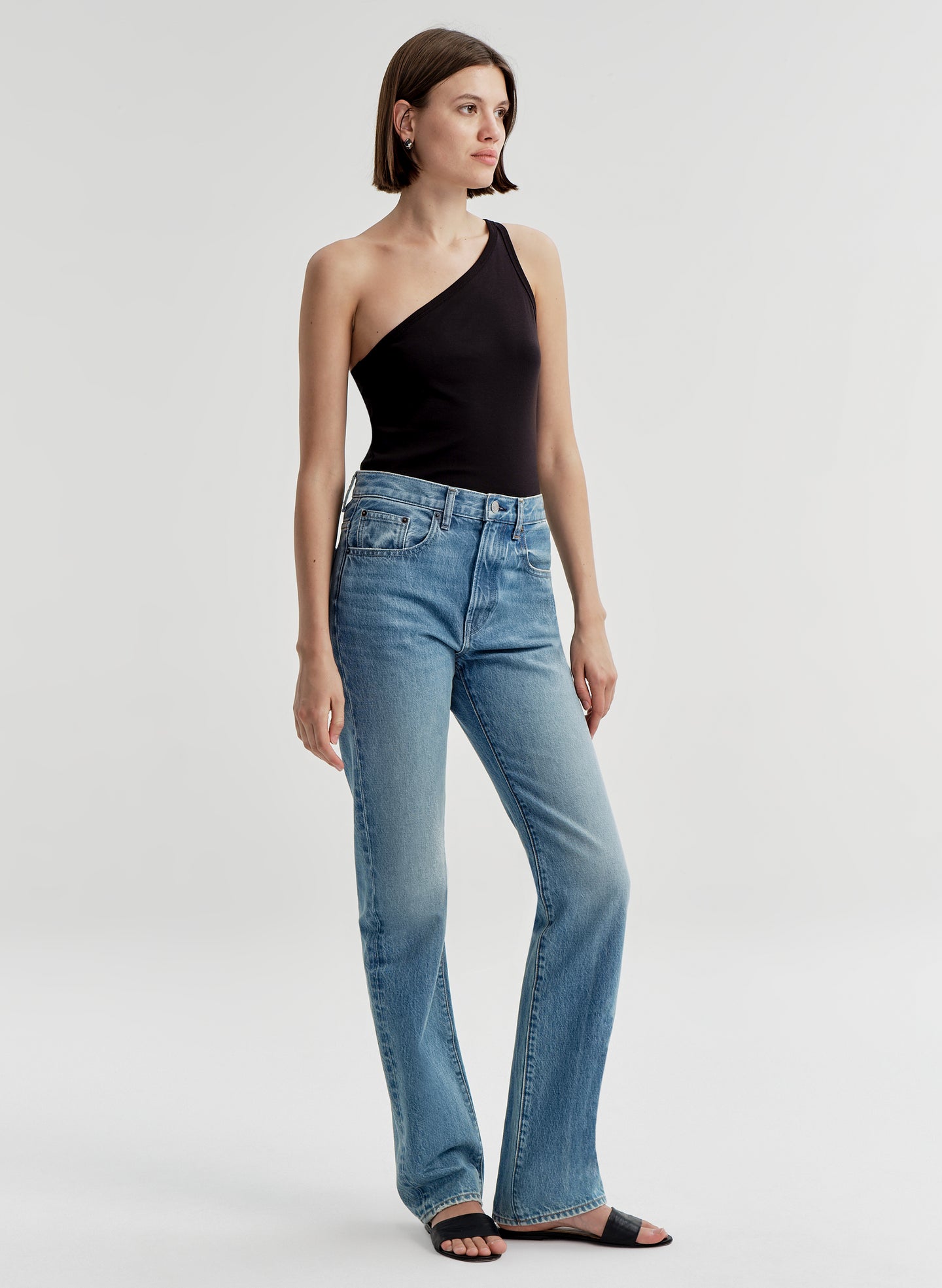 Woman wearing a black one-shoulder top and blue jeans on a light gray background