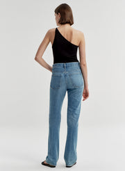 Woman wearing a black one-shoulder top and blue jeans on a light gray background